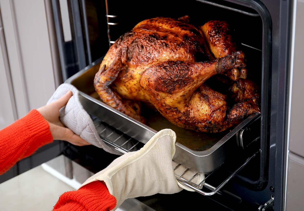 Person removes a roasted turkey from the oven using oven mitts